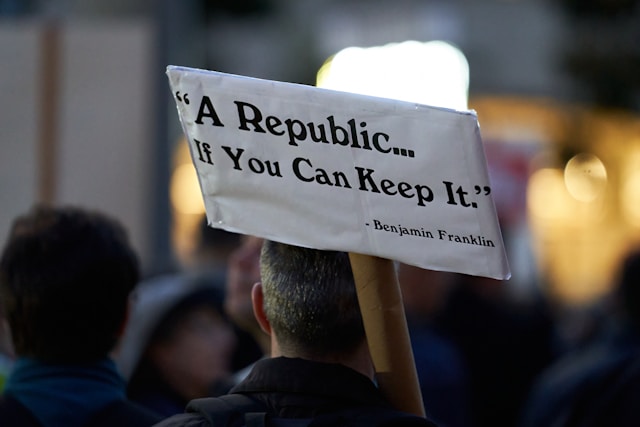 The back of a demonstrator holding a sign with a Ben Franklin quote “A Republic…If You Can Keep It”